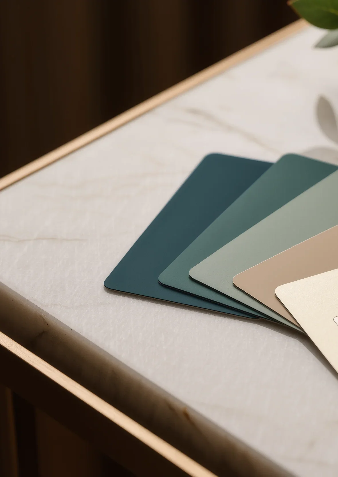A fan of matte bank cards in petrol, sage and warm sand tones on a sunlit marble surface